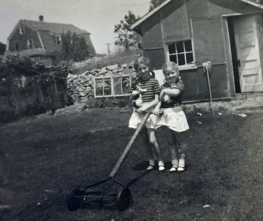 My sister and I with our pet kitties around 1945.  Don't remember actually mowing the law.  Notice the grape vines and the makeshift plant-starter in the background.  The little shed was where we canned our tomatoes.  This was taken at our home in Westerly, RI.