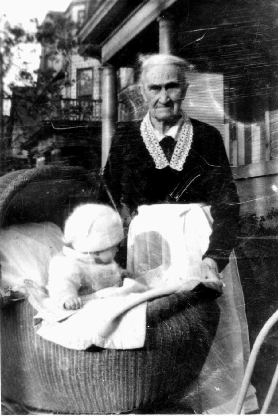 Ann Sullivan O’Brien at age 88  yrs of age (1837-1928) posing with her great grandson, John James O’Brien in his wicker buggy.  Ann was a devout Catholic, and in later years, could often be found praying her rosary on her front porch.  
Ann was born in Cobb Ireland and immigrated in May 1849 with her family.